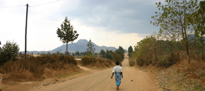 a young girl walks down a dirt road with power lines overhead